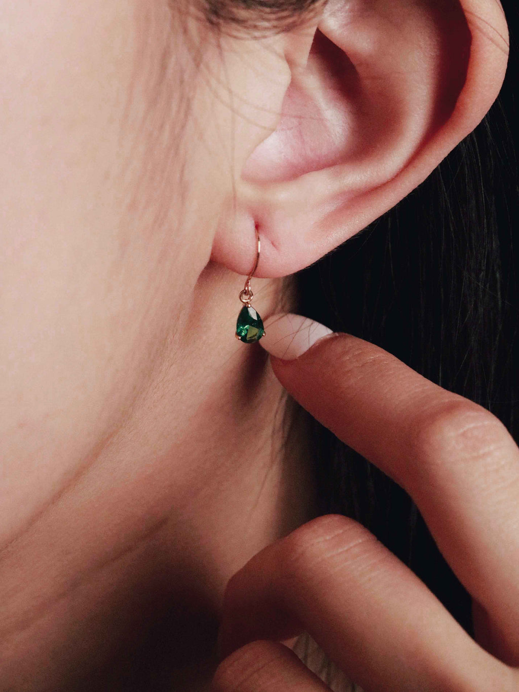 Close-up of a person wearing a green gemstone earring with a finger pointing to it.