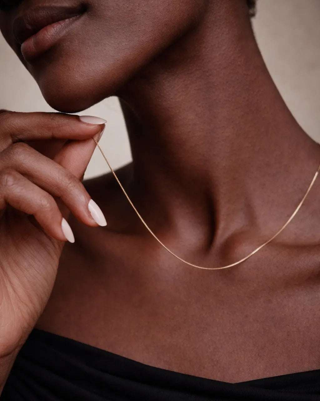 Close-up of a person wearing a delicate gold necklace against a neutral background