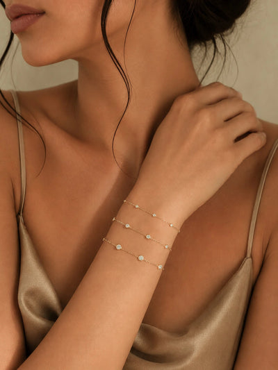 Three 18K solid gold diamond station bracelets in different sizes stacked on wrist, showing small medium and large bezel-set diamond variations