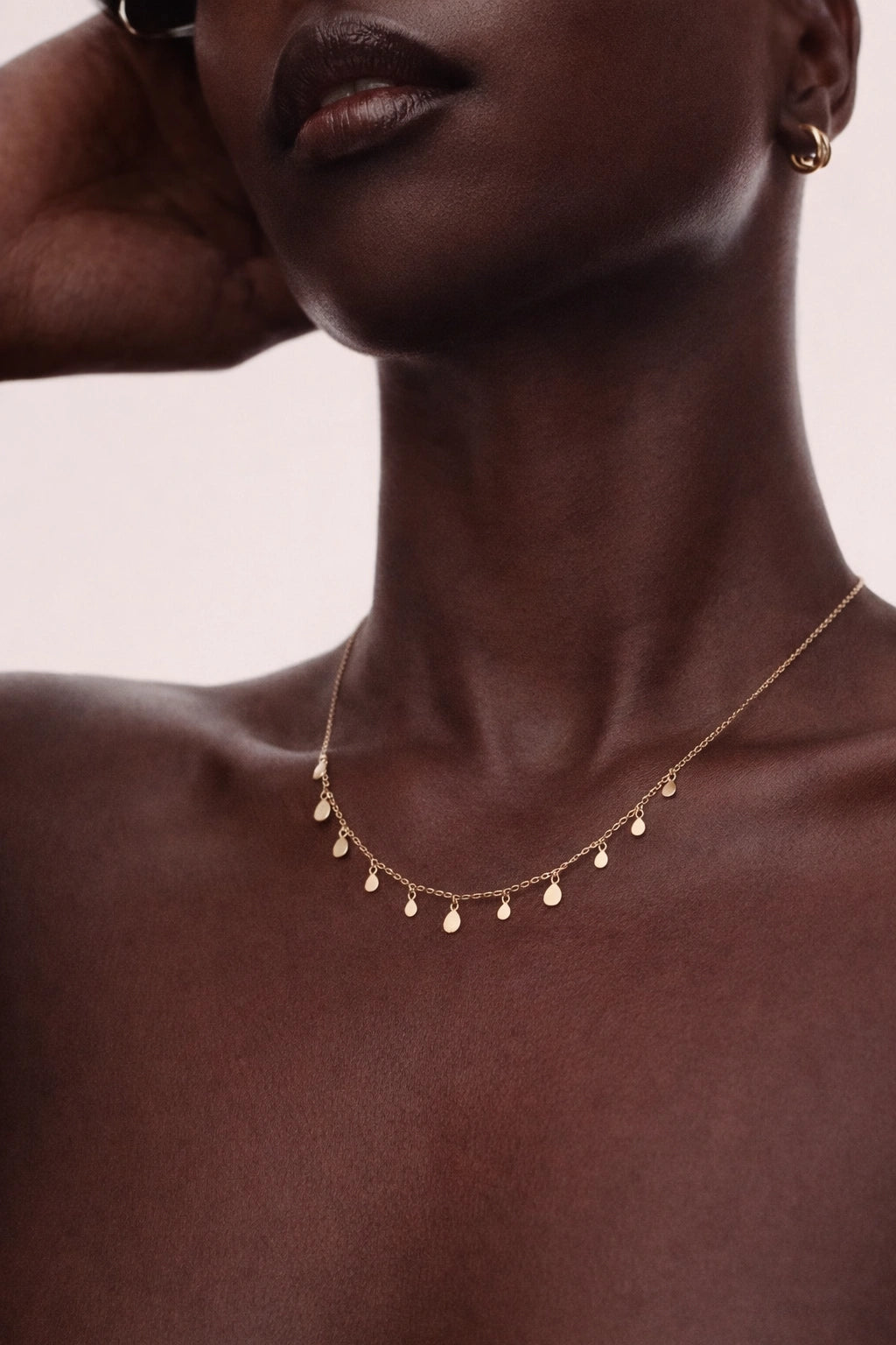 Close-up of a person wearing a delicate gold necklace with small beads on a neutral background