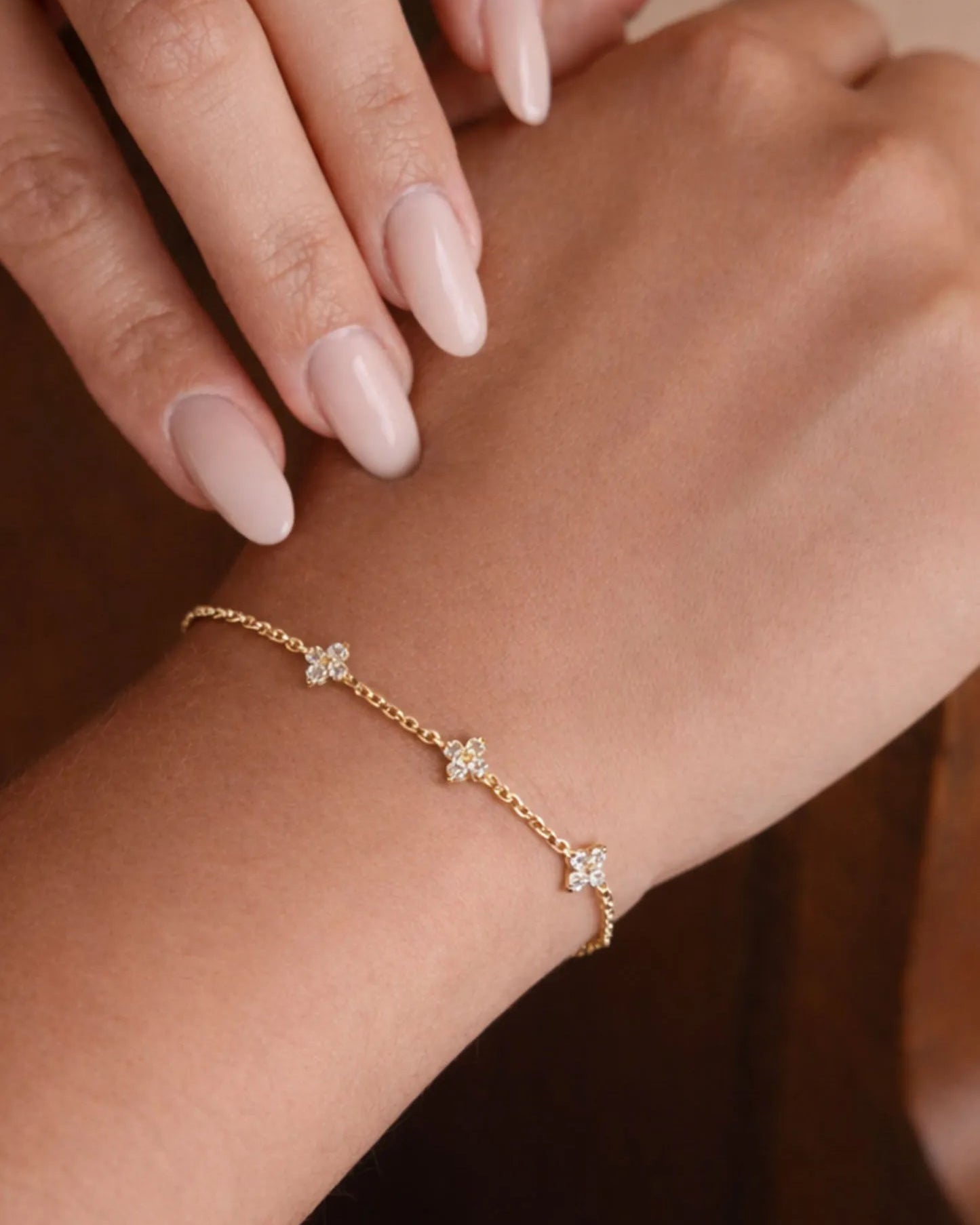 Gold bracelet with floral charms on a wrist against a neutral background