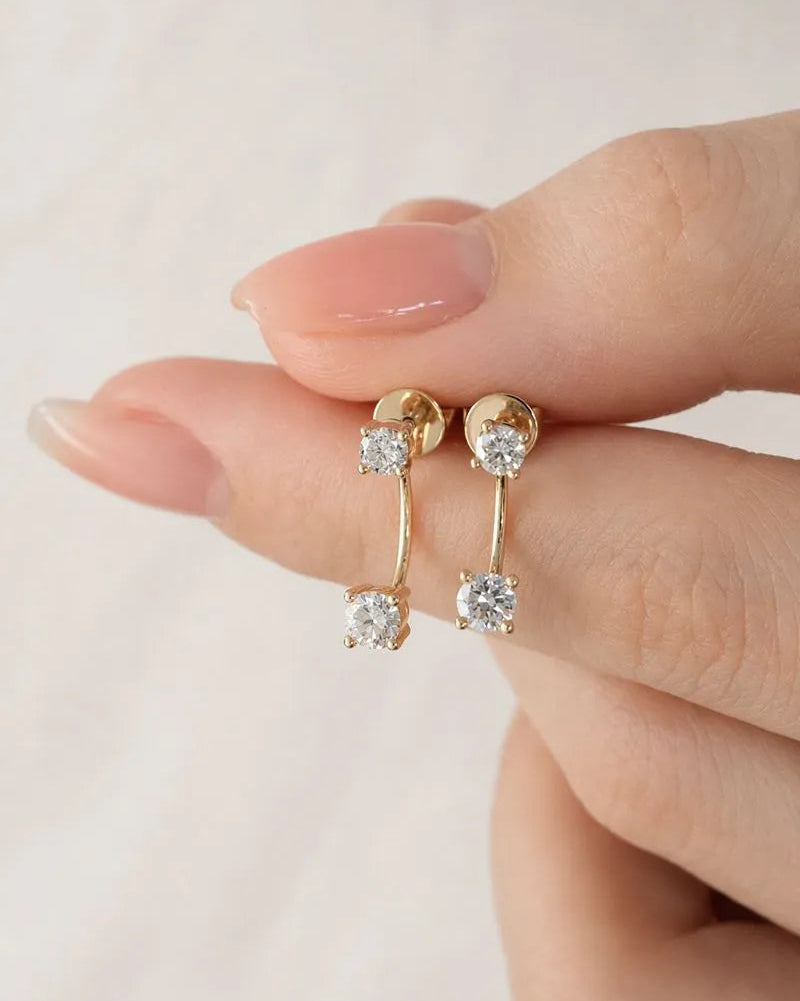 Gold earrings with clear gemstones held between fingers on a light background