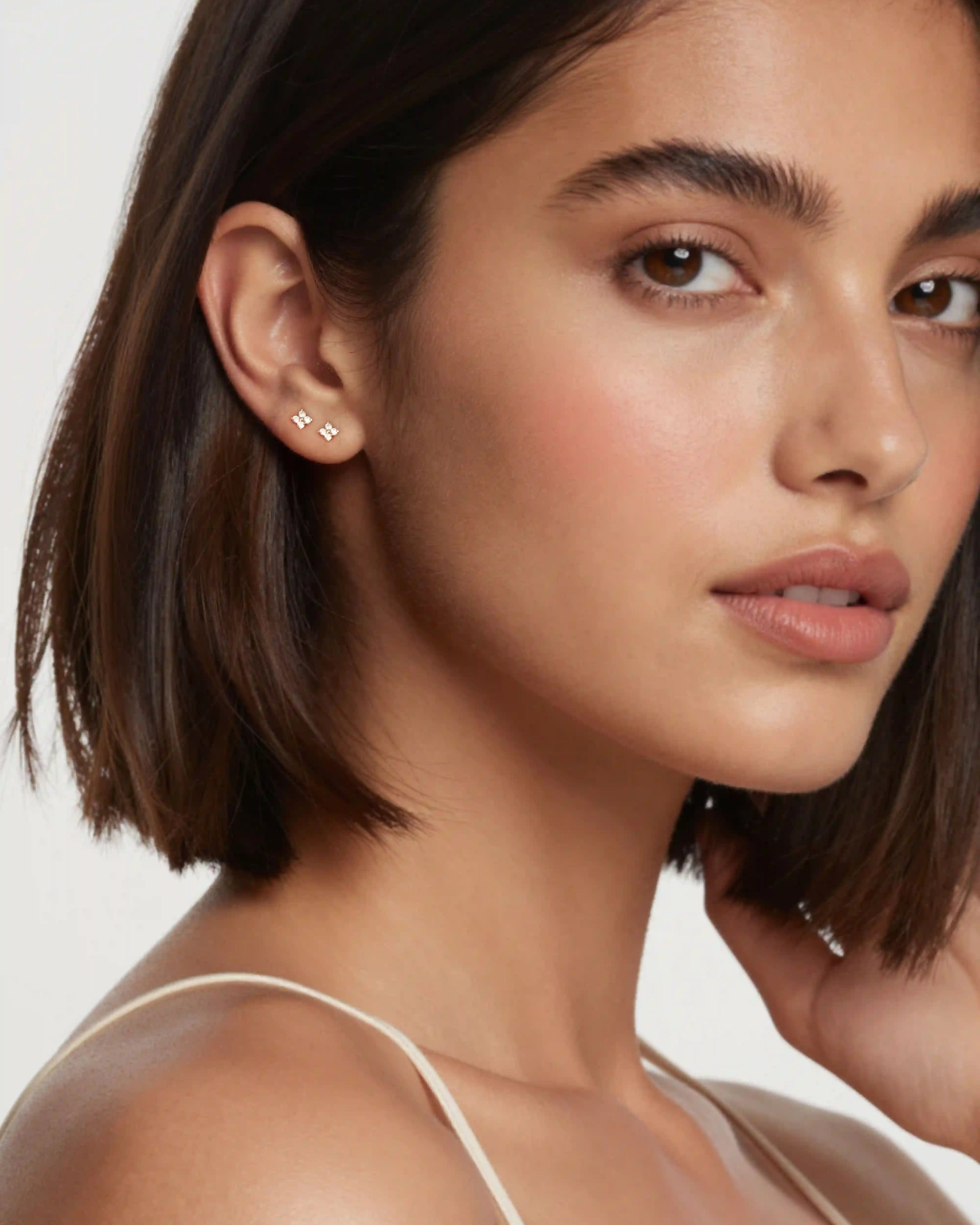Close-up of a woman wearing diamond stud earrings with a plain background