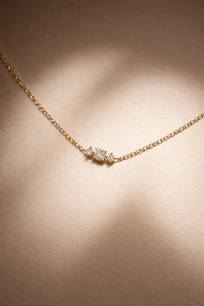 Rose gold necklace with three diamonds on a beige background