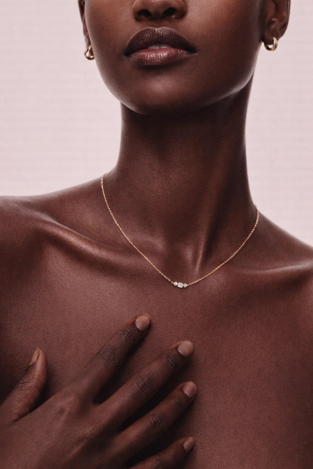 Close-up of a person wearing a delicate necklace with a soft pink background