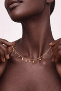 Close-up of a person wearing a delicate gold necklace against a soft pink background