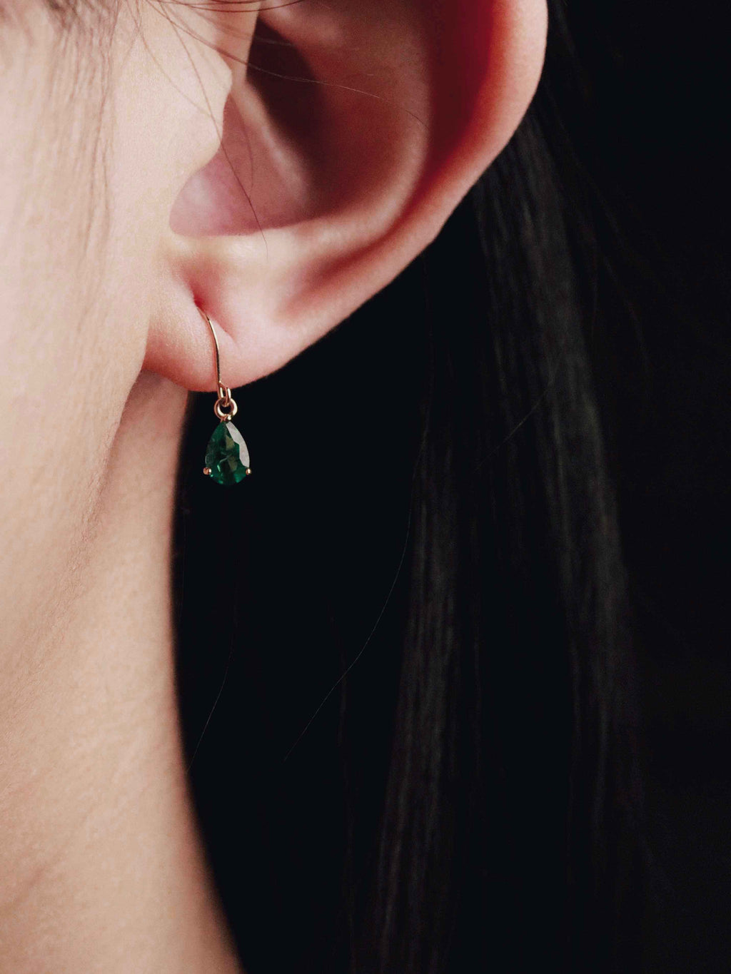 Close-up of an ear wearing a green gemstone earring with a dark background