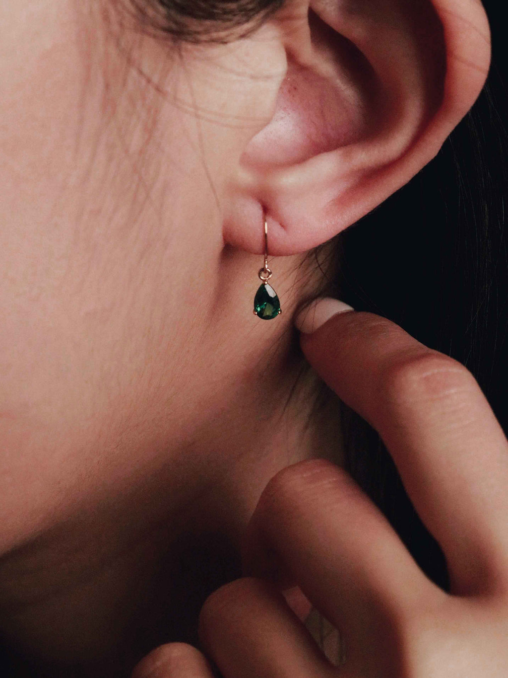 Close-up of a person wearing a green teardrop earring with a hand adjusting it.