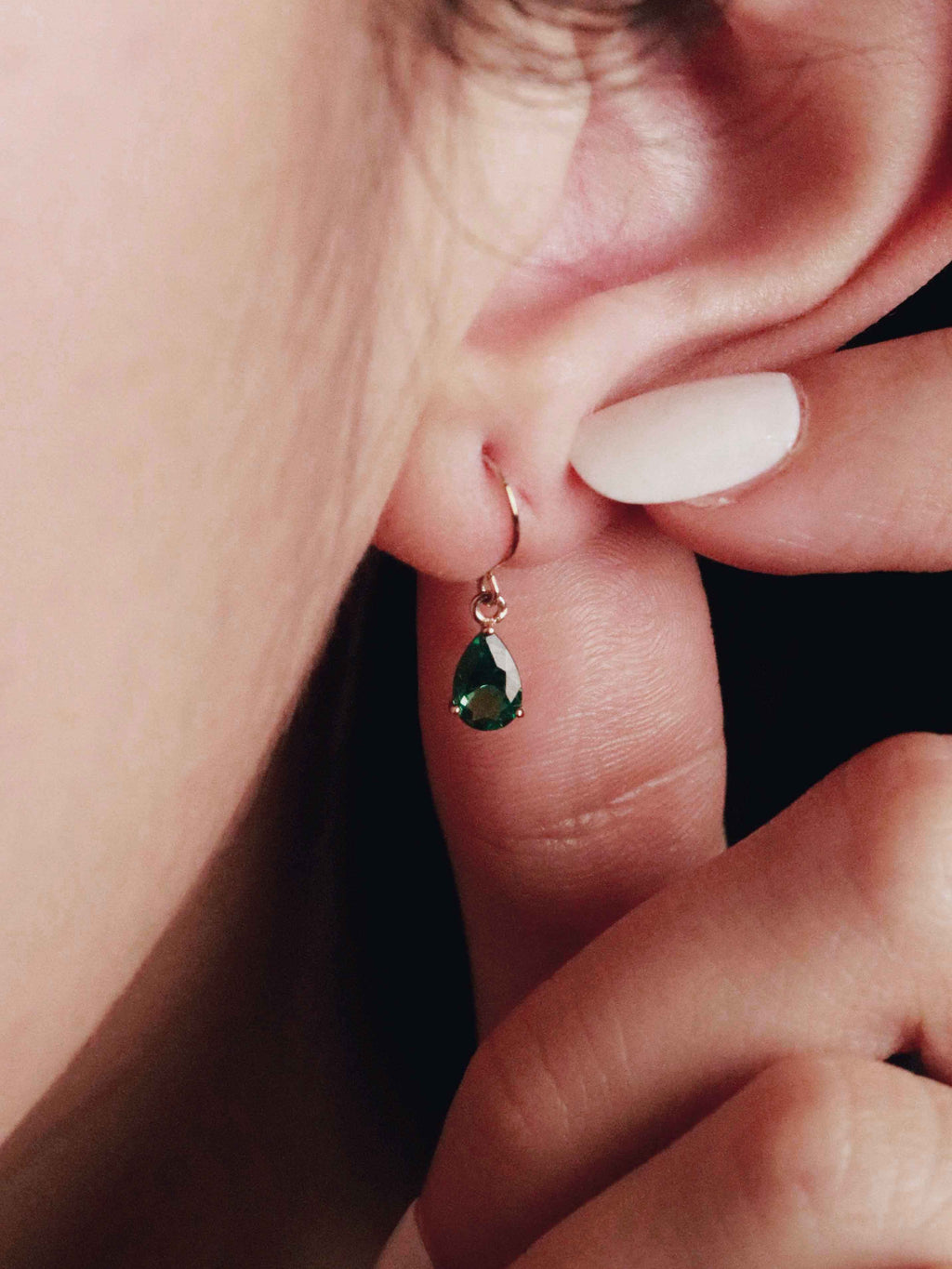 Close-up of a person wearing a green teardrop earring.