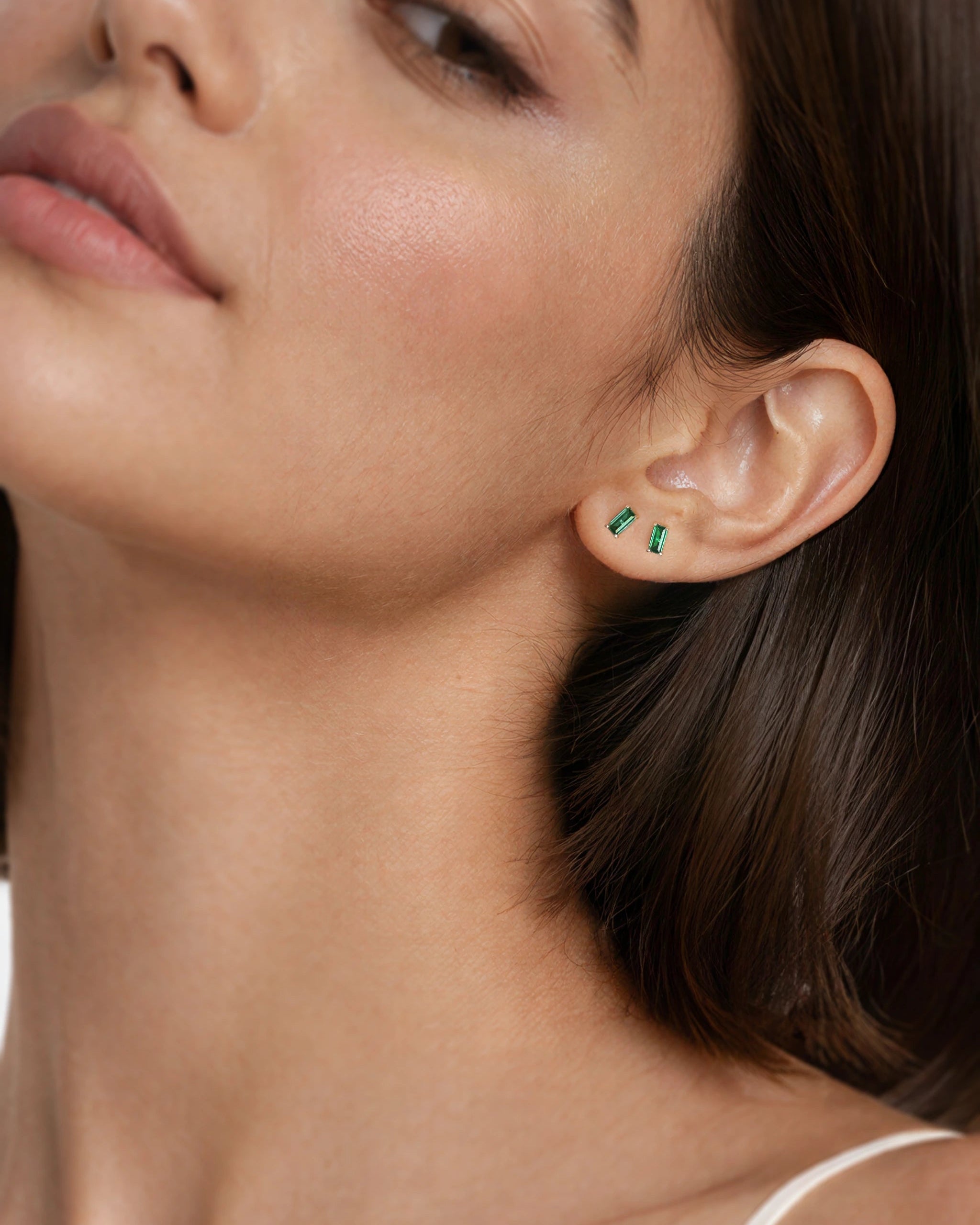 Close-up of a woman wearing green earrings with a neutral background