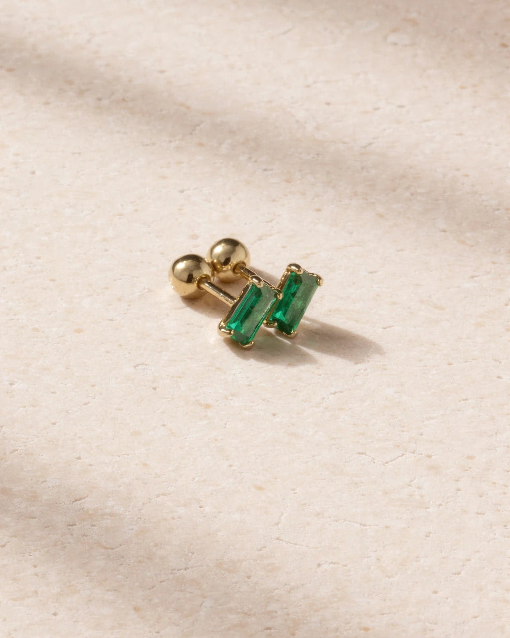 Gold earring with green gemstones on a beige fabric background
