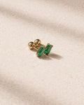 Gold earring with green gemstones on a beige fabric background