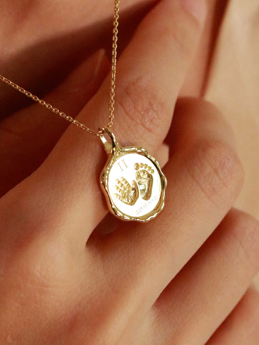 Gold necklace with a pendant featuring handprints and a date, held by a hand.