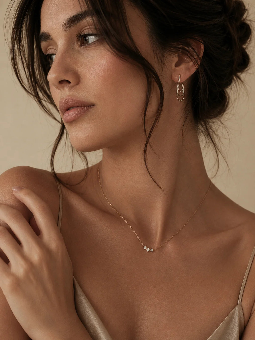 A close-up lifestyle shot of a woman wearing delicate jewelry, featuring a thin gold chain necklace with three small pearls and matching gold hoop earrings.