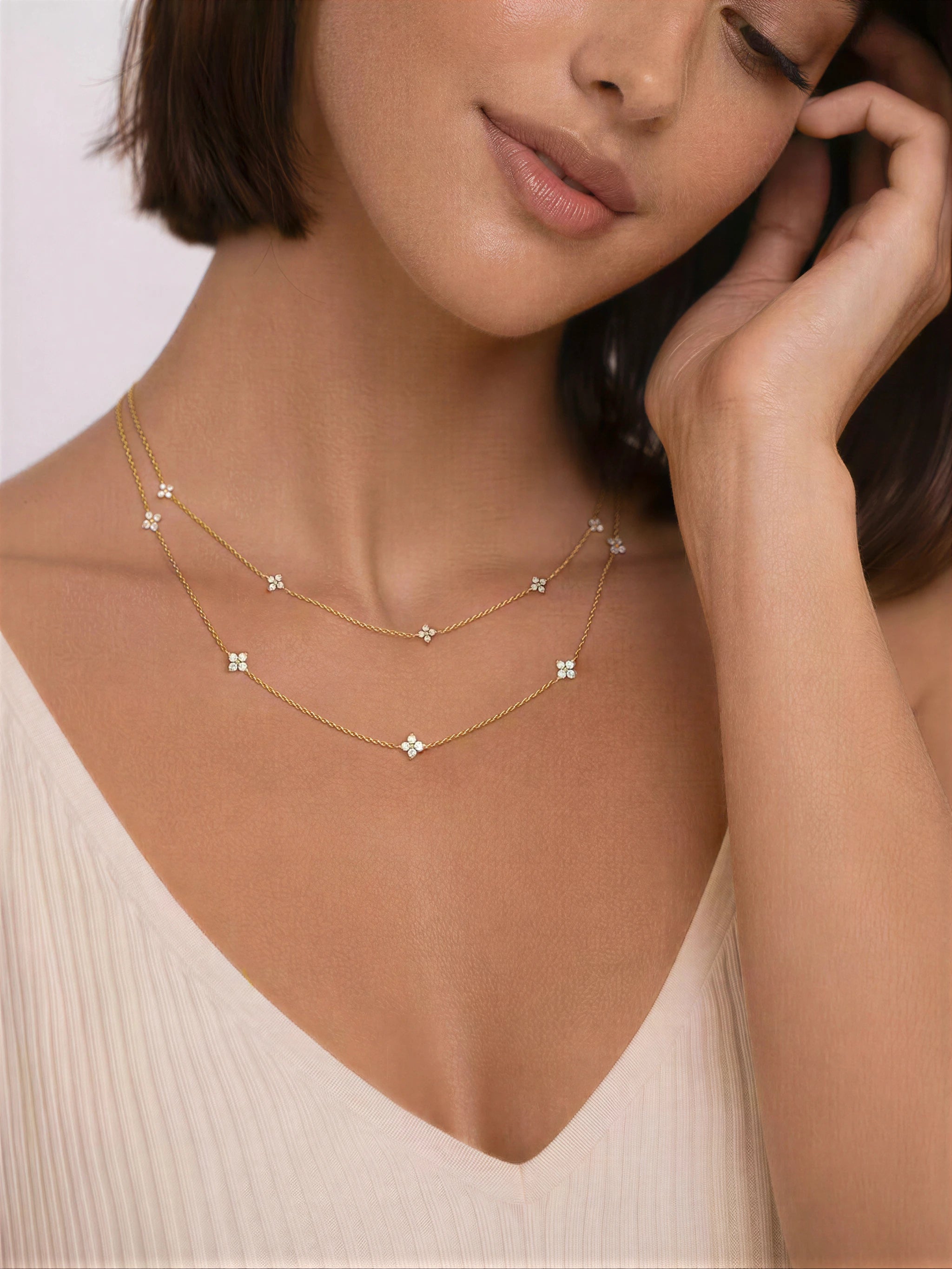 Woman wearing a delicate gold necklace with small diamonds on a plain background