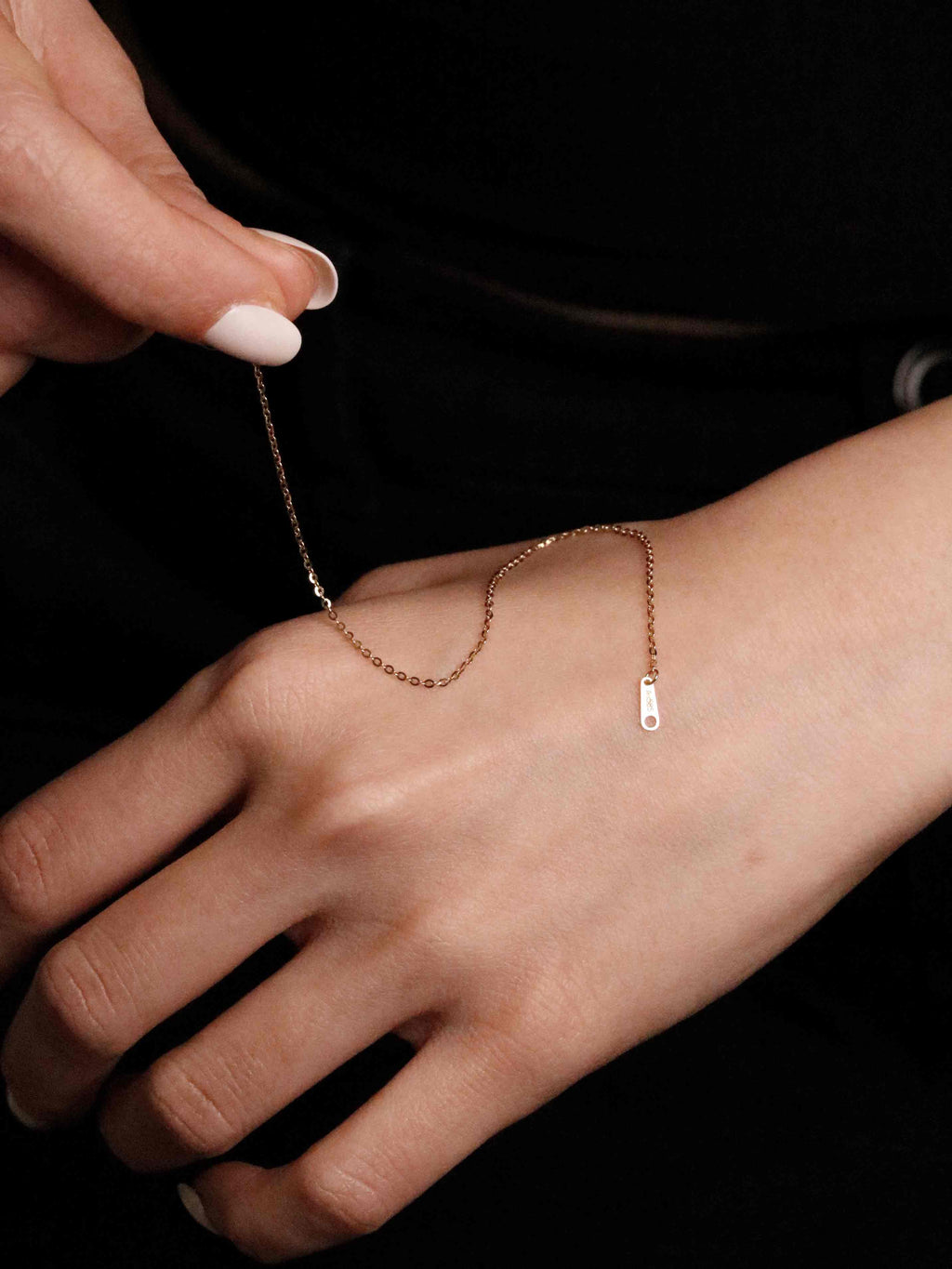 gold bracelet being adjusted on a wrist against a black background