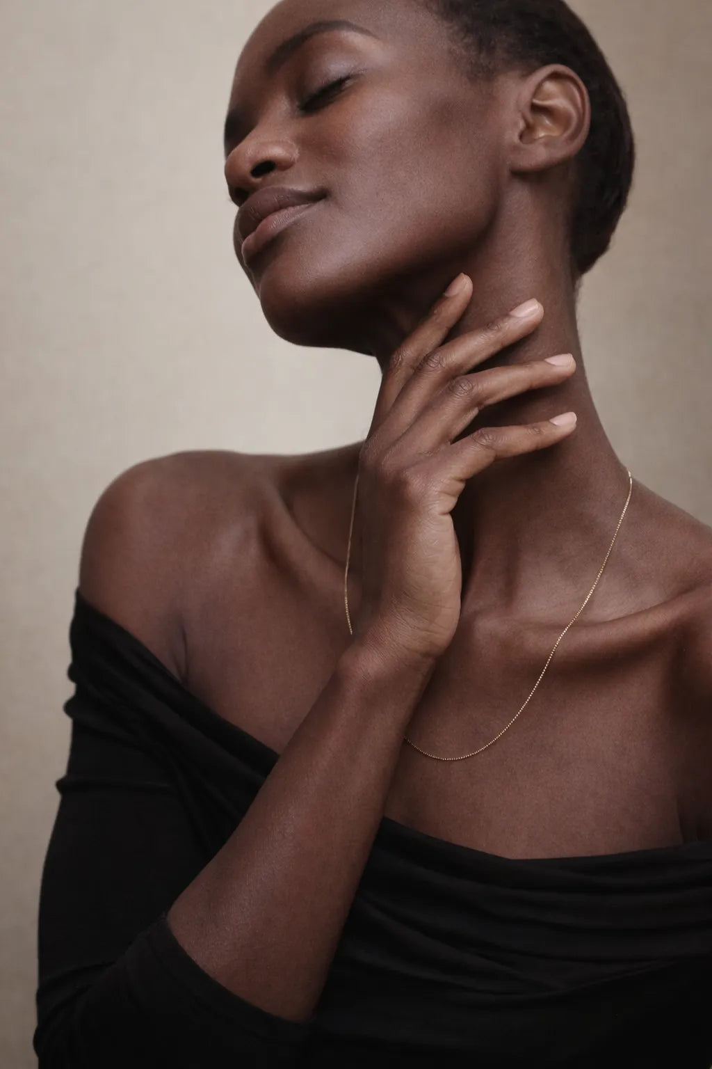 Woman wearing a gold necklace against a neutral background