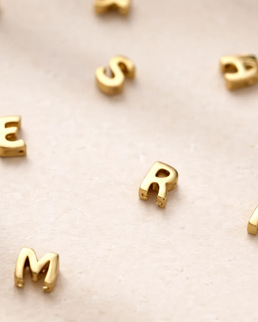 Gold letter beads spelling 'E R M' on a beige background