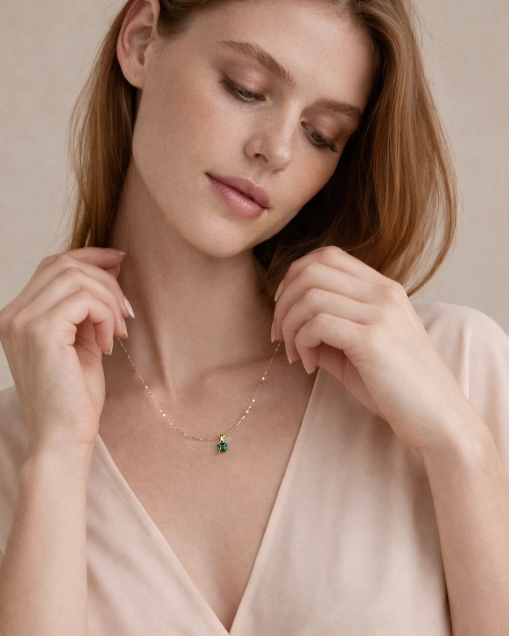 Woman wearing a delicate necklace with a green pendant against a neutral background