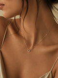 A delicate gold necklace with a small crescent moon pendant worn by a model in a warm, close-up lifestyle shot.