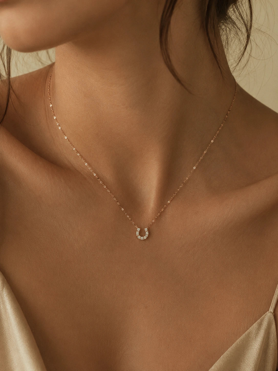 A delicate gold chain necklace with a small crescent moon pendant set with clear stones, shown worn on a model's neck.