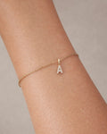 Gold bracelet with a letter 'A' charm on a wrist against a neutral background