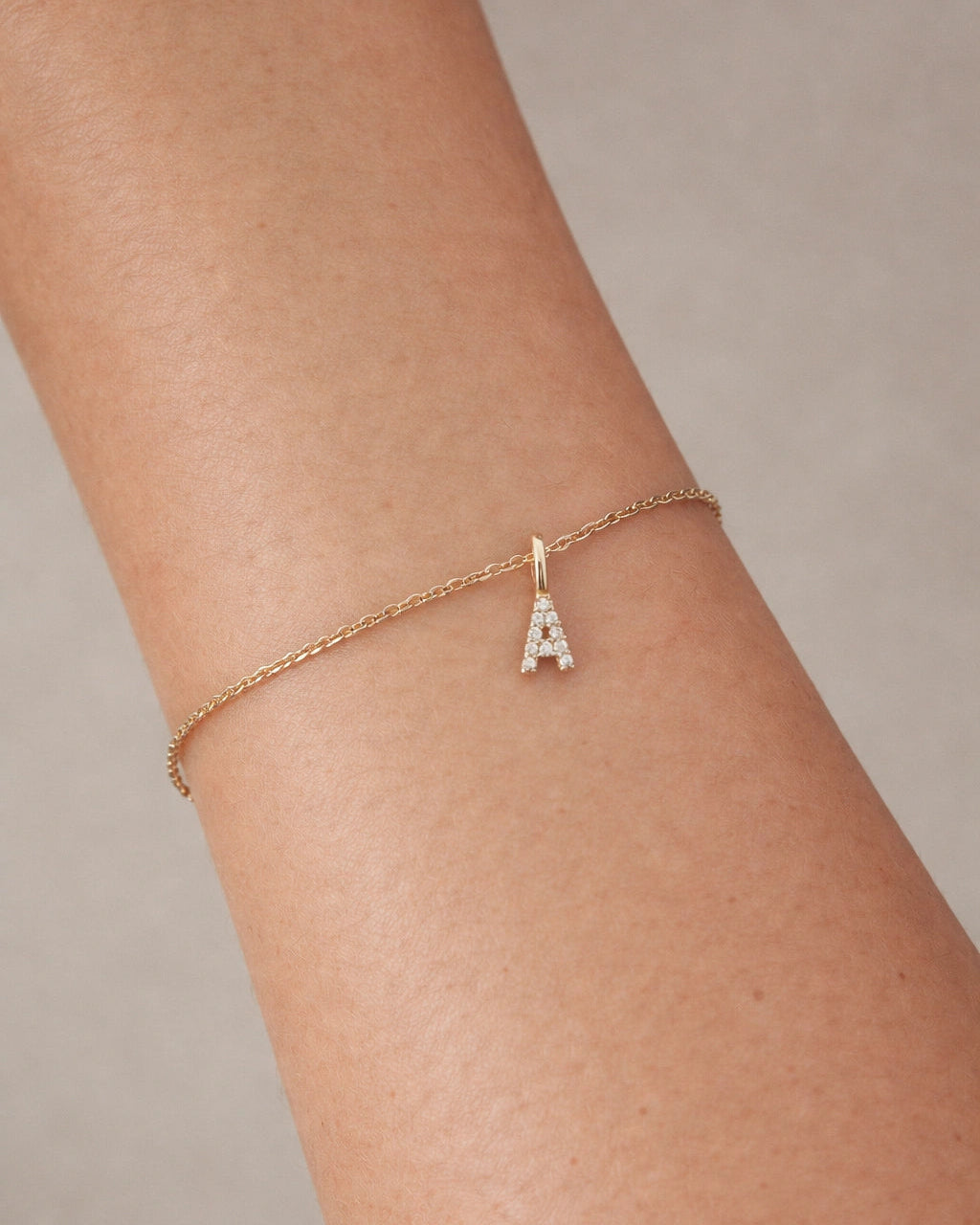 Gold bracelet with a letter 'A' charm on a wrist against a neutral background