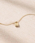 Gold necklace with a small pendant on a beige fabric background