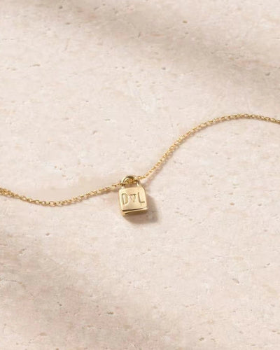 Gold necklace with a small pendant on a beige fabric background