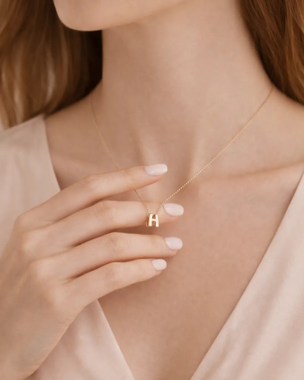 Gold necklace with a small 'H' pendant worn by a person
