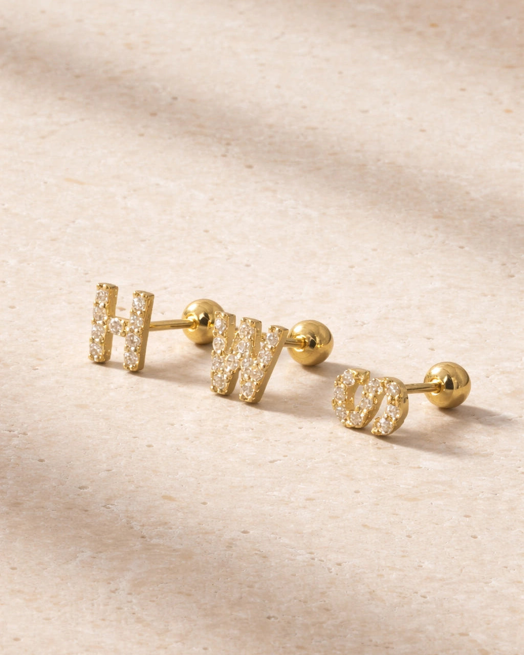 Gold earrings with 'H' and 'W' on a beige fabric background