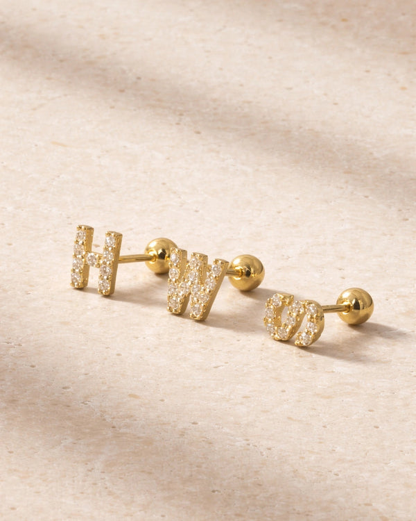 Gold earrings with 'H' and 'W' on a beige fabric background