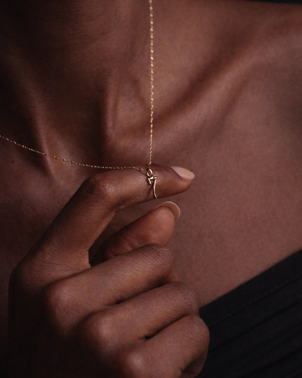 Close-up of a hand wearing a gold ring with a delicate necklace against a dark background