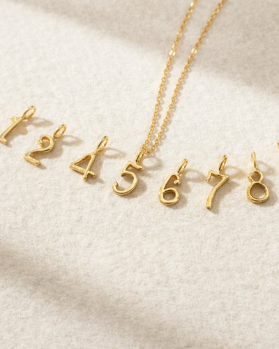 Gold necklace with number pendants on a light beige background