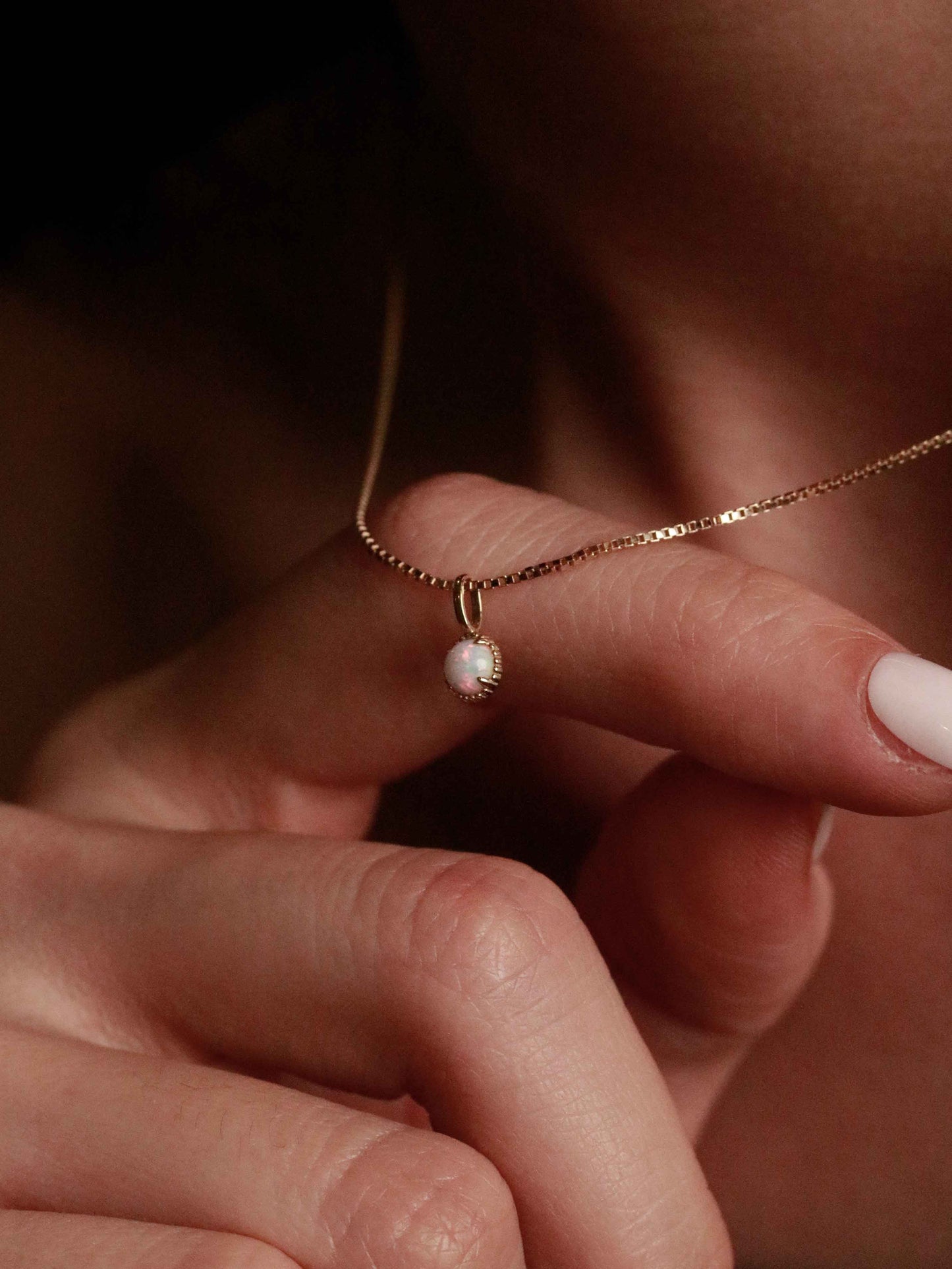 Close-up of a hand holding a delicate gold necklace with a small pendant.