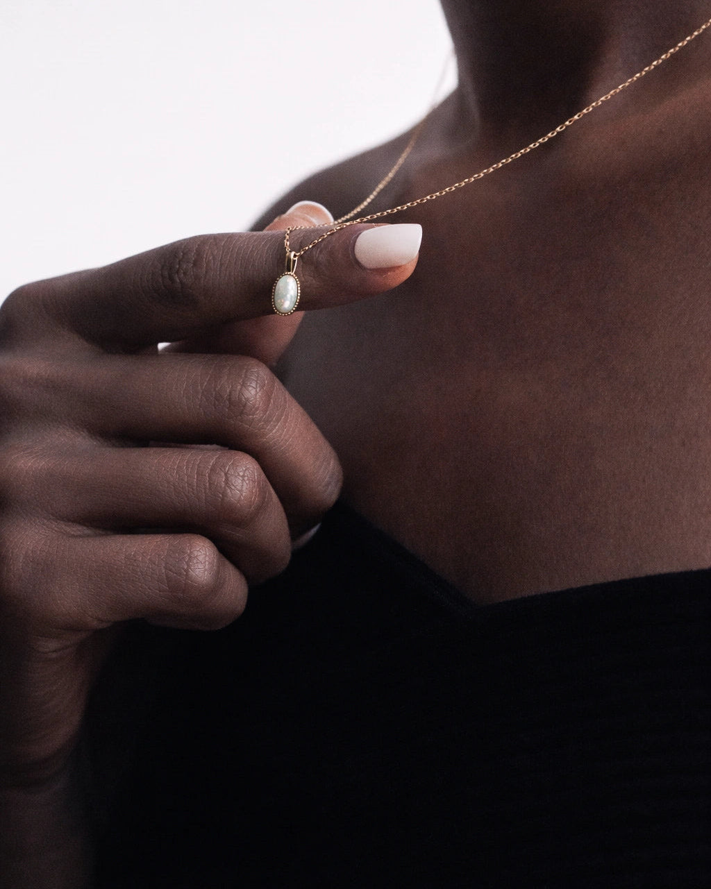 Person wearing a delicate necklace with a small pendant, close-up of hand and neck.