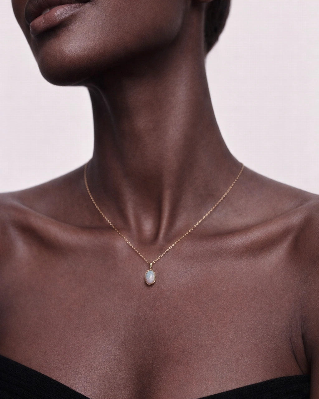 Close-up of a necklace with a pendant on a model against a light pink background