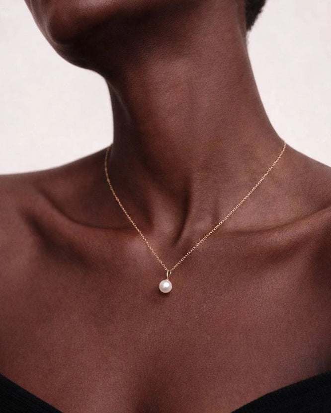 Necklace with a pearl pendant worn by a model against a neutral background