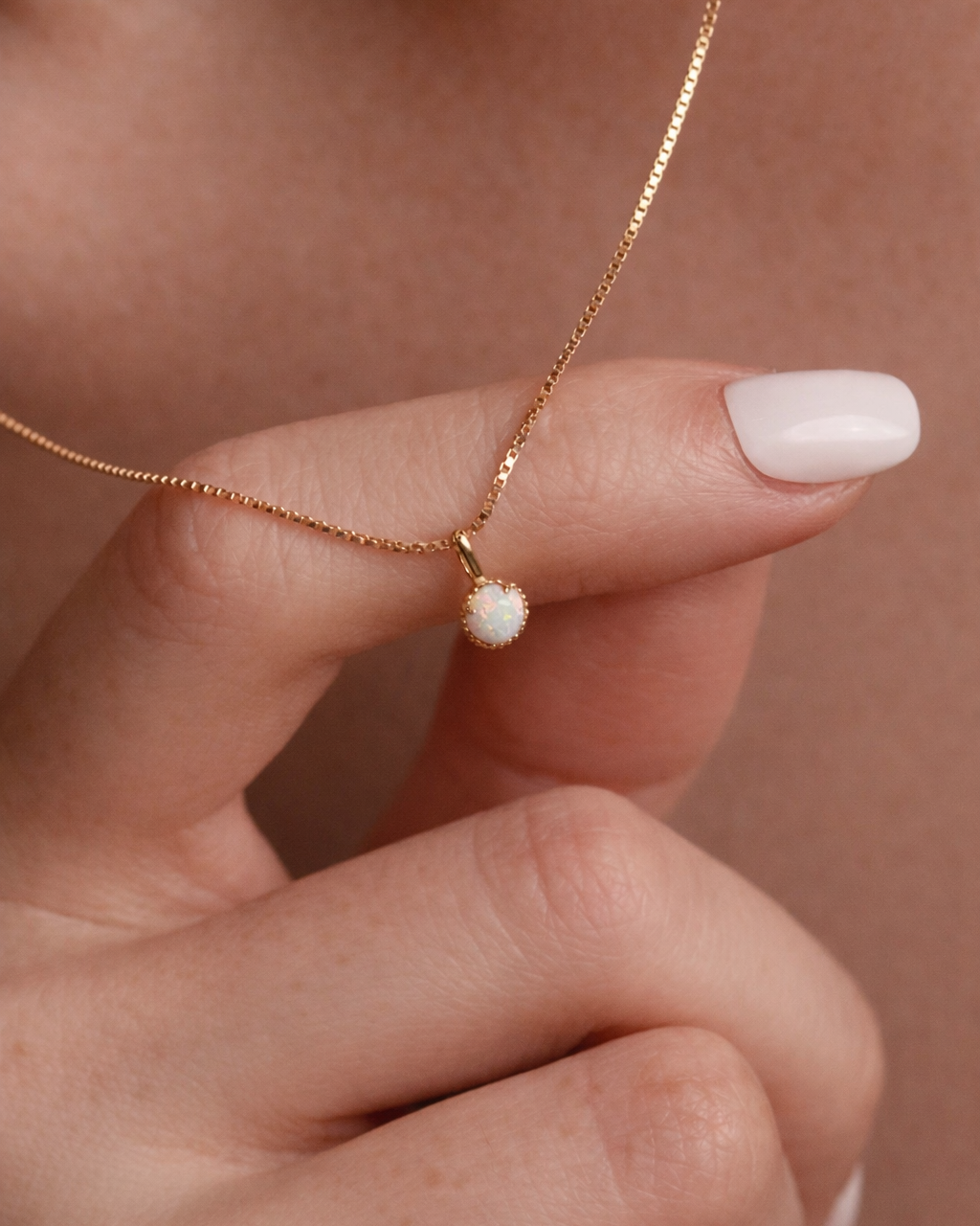Gold necklace with a small white pendant held by a hand against a neutral background