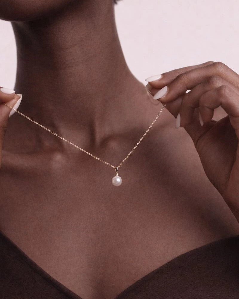 Necklace with a pearl pendant worn by a person against a neutral background