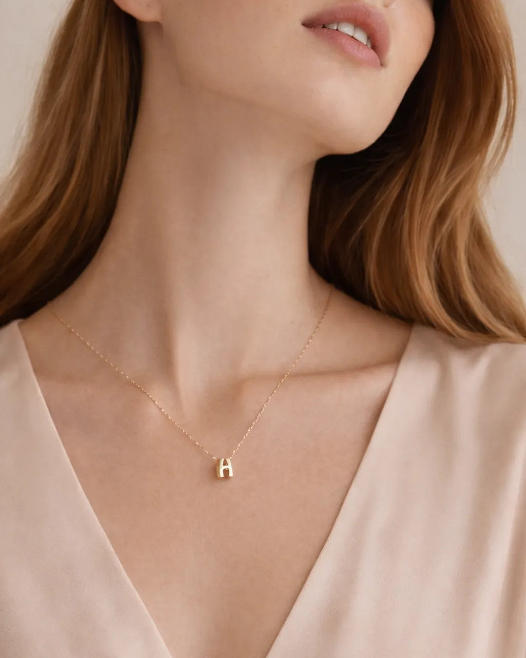 Woman wearing a gold necklace with a 'H' pendant on a beige background