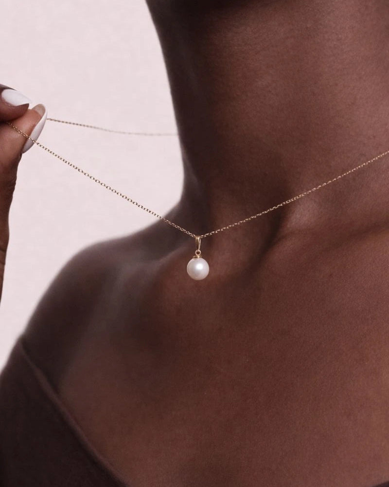 Pearl necklace being worn on a person's neck with a soft pink background