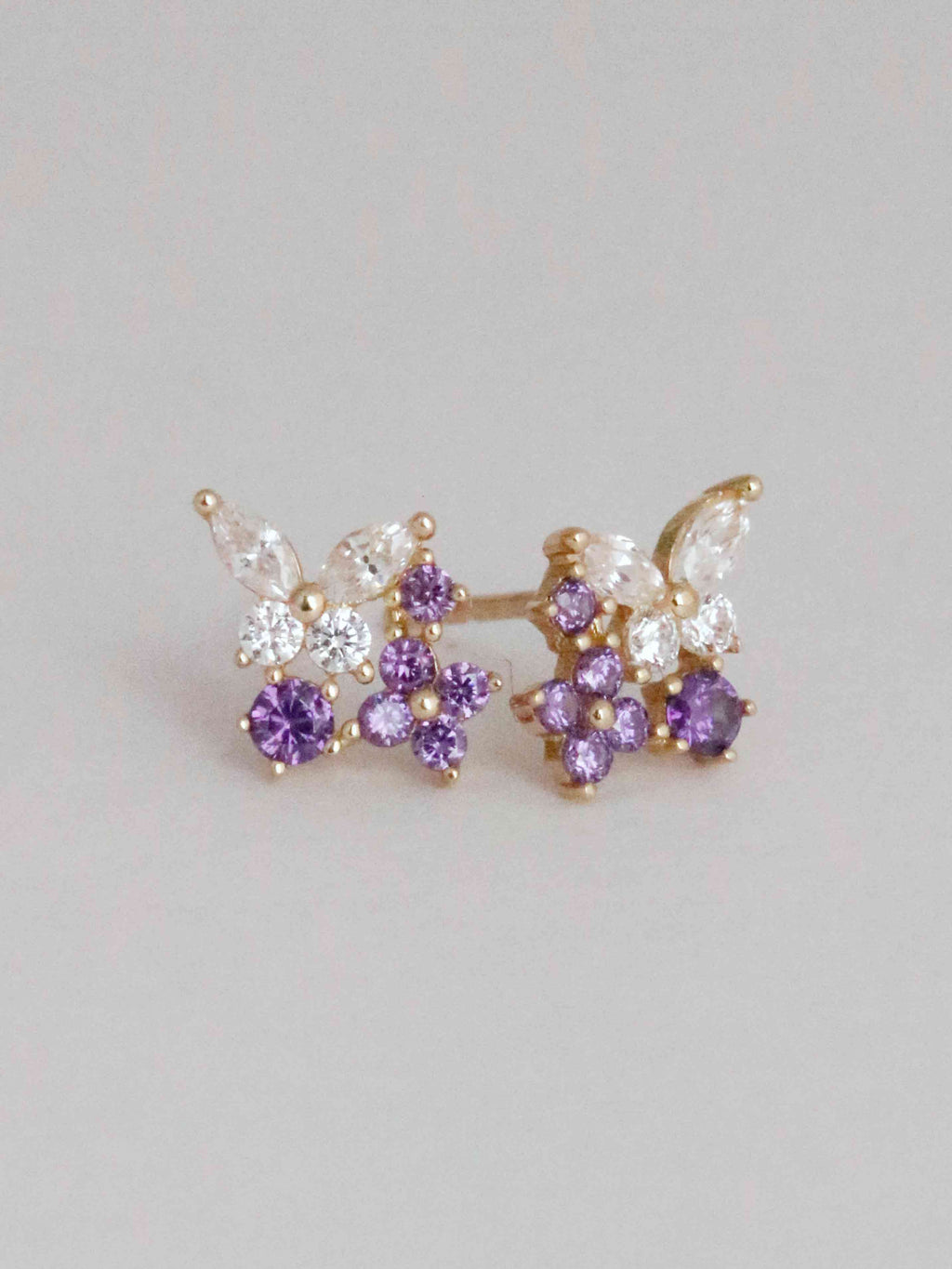 Butterfly-shaped earrings with purple and clear gemstones on a light gray background