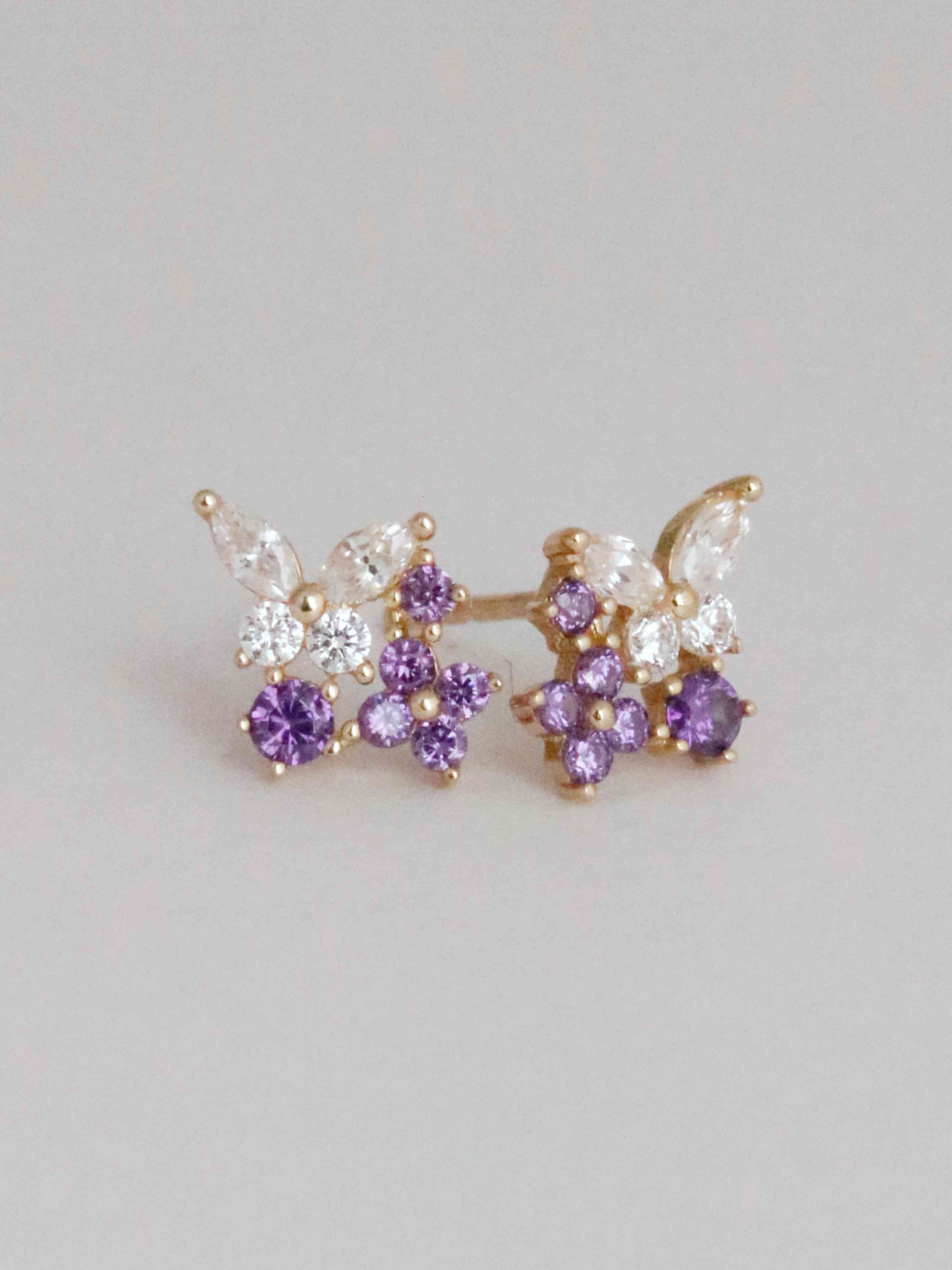 Butterfly-shaped earrings with purple and clear gemstones on a light gray background