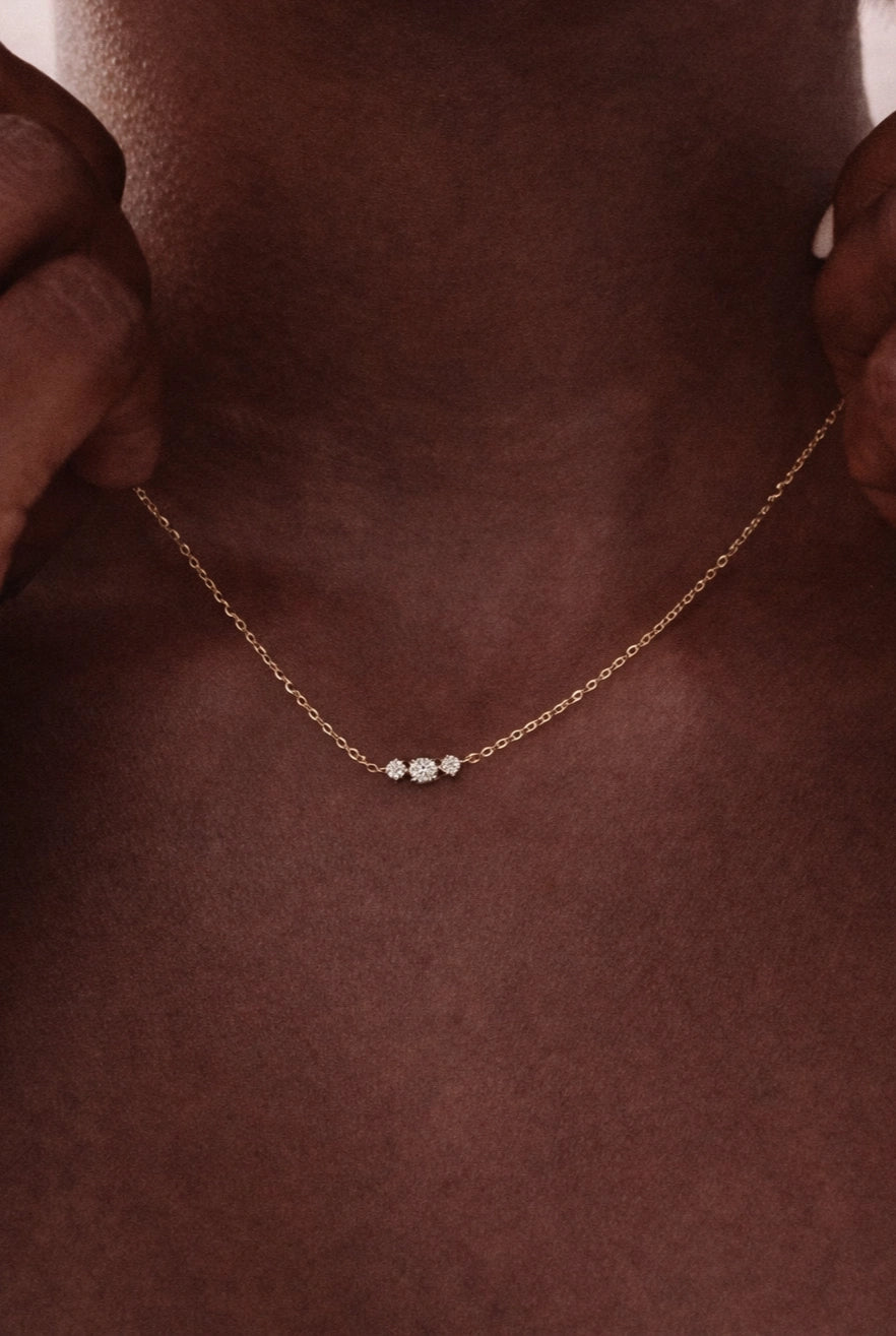 Gold necklace with three small diamonds on a person's neck against a brown background